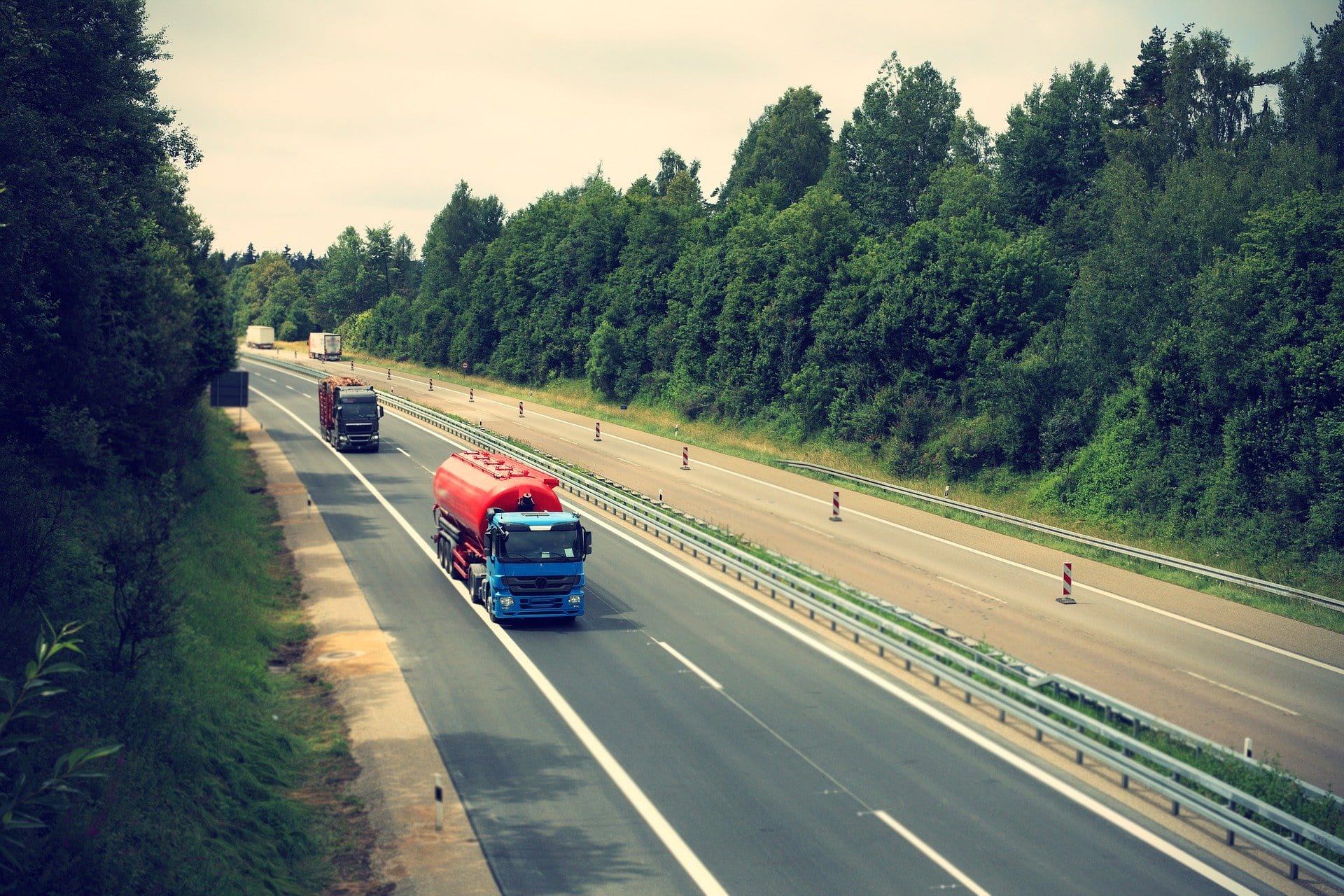LKW in den Farben Rot und Blau fährt bei bewölktem Wetter auf einer Autobahn