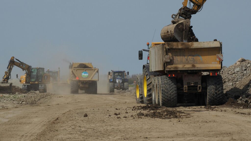 Baustellenfahrzeuge fahren über eine staubige Fläche.