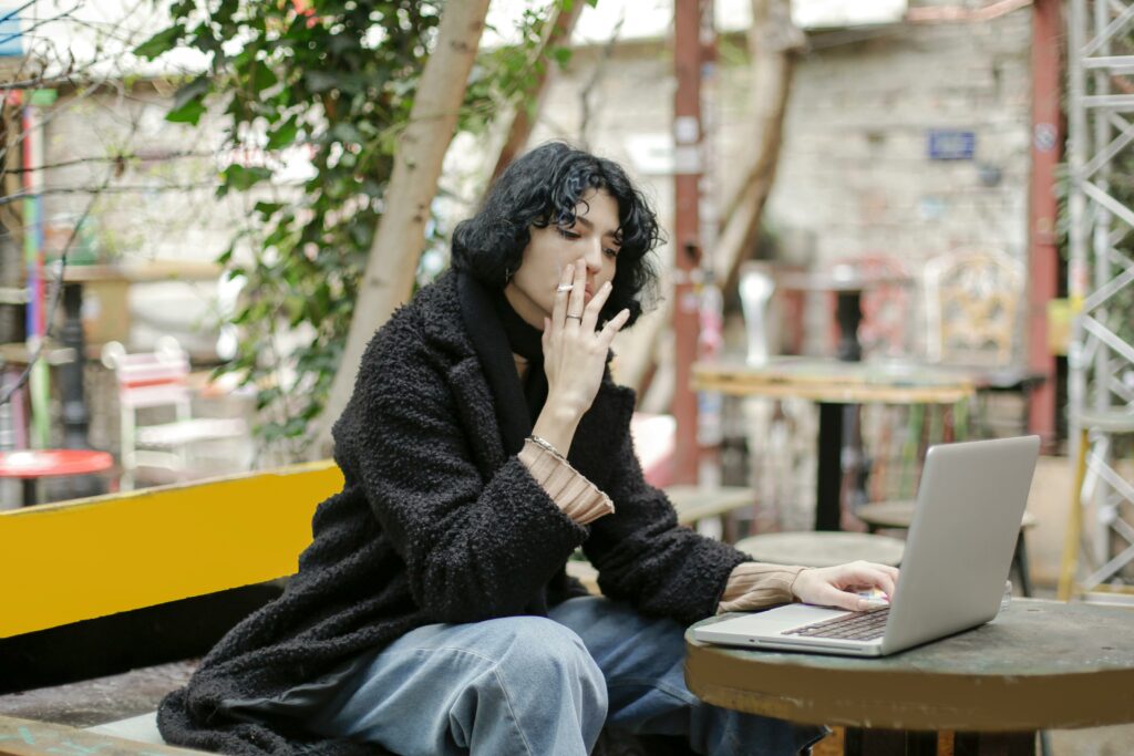 Eine Frau raucht draußen bei der Arbeit vor ihrem Laptop.